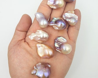 May include: A selection of iridescent baroque pearls in diverse shapes and sizes, with colours including cream, lavender, and gold. The pearls are held in a hand against a white backdrop, highlighting their unique textures.
