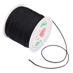 May include: A spool of black waxed cord with a white label that says "珠圆玉润" in Chinese characters. The cord is unwound and laid out on a white background.