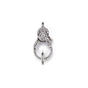May include: Silver-toned clasp with a clear crystal design. The clasp is oval-shaped and has a small, clear crystal in the center.