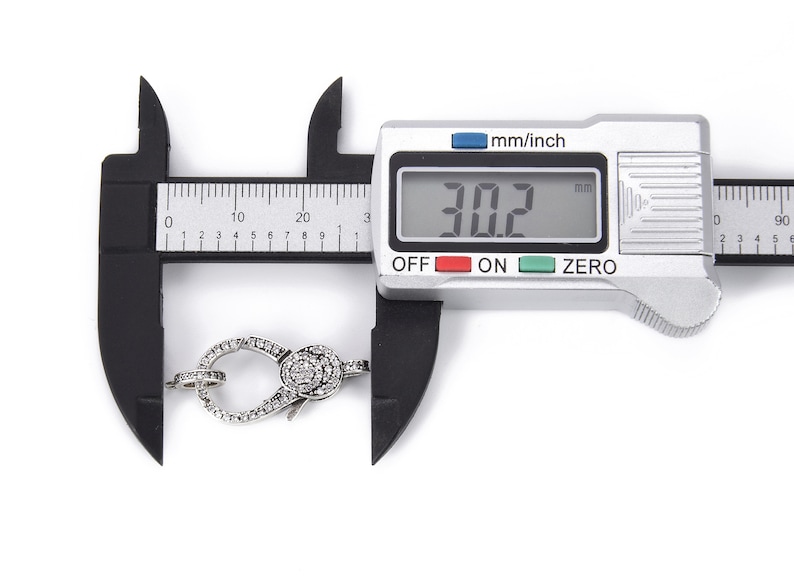 May include: A silver-toned clasp with clear sparkling stones is measured with a digital caliper. The caliper reads 30.2 mm.