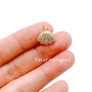 May include: A gold-colored seashell pendant with a small loop at the top. The pendant is encrusted with small, clear gemstones. The seashell design is detailed and has a polished finish.