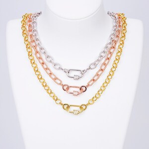 K&ouml;nnte beinhalten: Drei goldene Kettenhalsb&auml;nder mit einem Verschluss. Die Ketten sind &uuml;bereinander gelegt. Die oberste Kette ist silber, die mittlere Kette ist ros&eacute;gold und die unterste Kette ist gold. Jeder Verschluss hat ein kleines Quadrat aus klaren Zirkonia-Steinen.