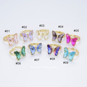 May include: Nine gold butterfly rings with different colored crystal accents. The rings are numbered 01 through 09.