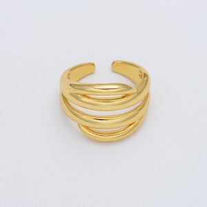 May include: A gold-toned ring with a multi-layered design. The ring is made of smooth, rounded metal and has a simple, modern style.