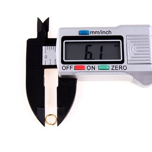 May include: A silver digital caliper with a black ruler and a black jaw. The caliper is measuring a small gold ring. The digital display reads "6.1 mm".