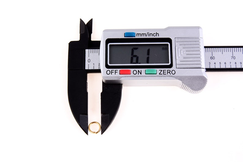 May include: A silver digital caliper with a black ruler and a black jaw. The caliper is measuring a small gold ring. The digital display reads "6.1 mm".