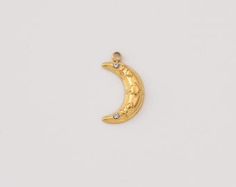 May include: A gold-colored crescent moon pendant with star and crystal accents. The pendant has a loop at the top for hanging and is likely made of metal. The moon shape is a popular design element in jewelry.