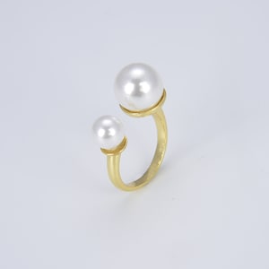 May include: A gold ring with two white pearl accents. The ring is open and has a simple design.