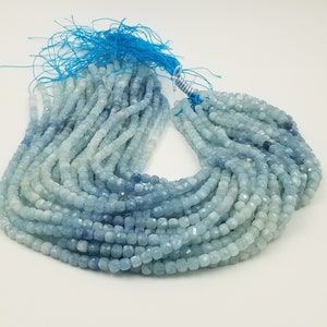 May include: Strands of faceted aquamarine beads in varying shades of blue and white. The beads are small, square-shaped, and strung together. A blue tassel is attached to the top of the strands. The beads are suitable for jewelry making.