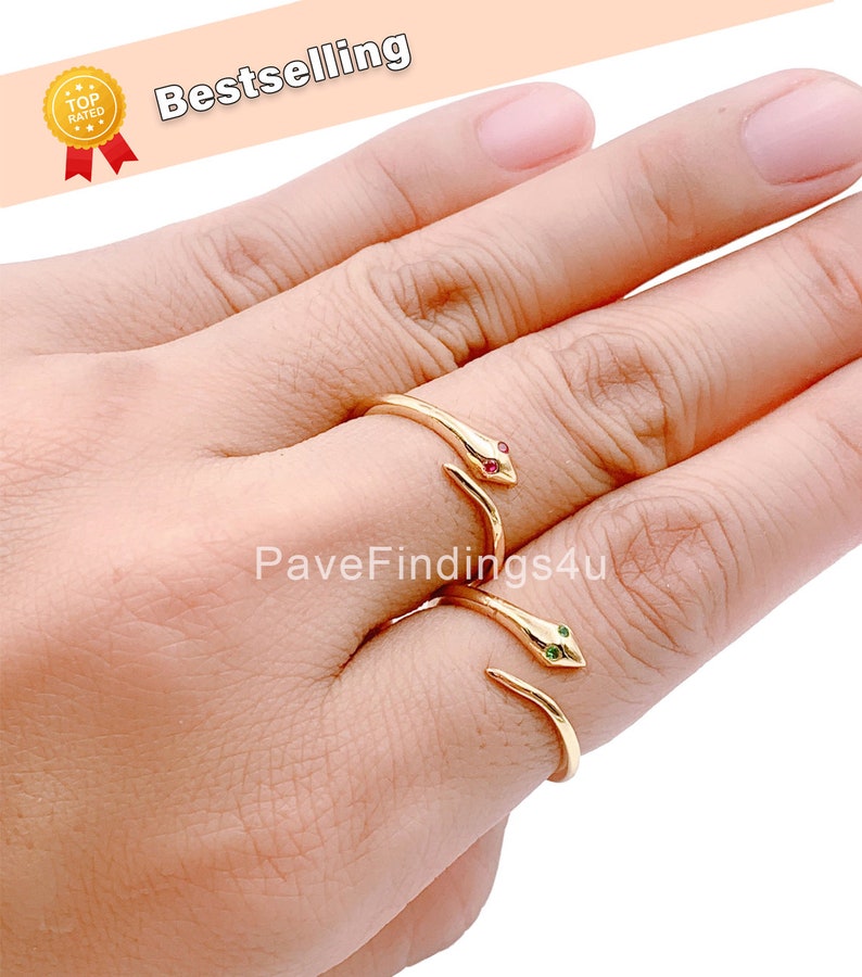 May include: Two gold snake rings with red and green gemstone eyes. The rings are adjustable and can be worn on any finger.