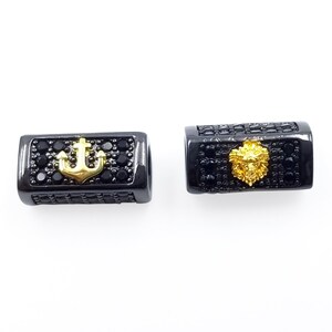 May include: Two black metal beads with gold accents. One bead features an anchor and the other features a lion's head.