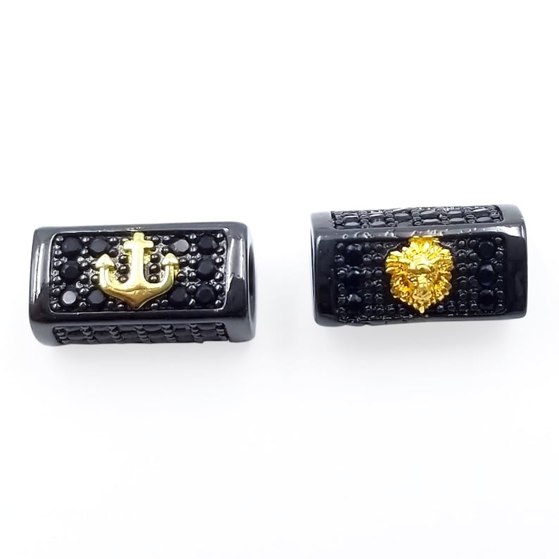 May include: Two black metal beads with gold accents. One bead features an anchor and the other features a lion's head.