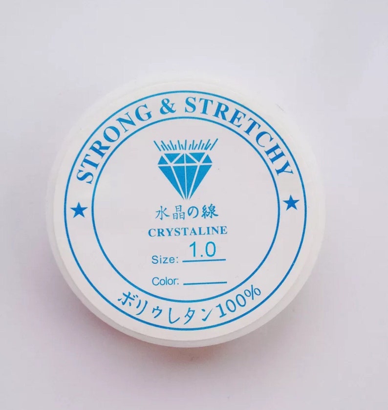 Puede incluir: Un recipiente redondo blanco con texto azul y un gr&aacute;fico de diamante azul. El texto dice "STRONG & STRETCHY", "水晶の線", "CRYSTALINE", "1.0", "Size:", "Color:" y "ボリウレタン100%".