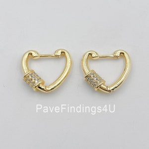 May include: A pair of gold heart-shaped hoop earrings with a small, clear crystal-encrusted cylinder accent on each hoop.