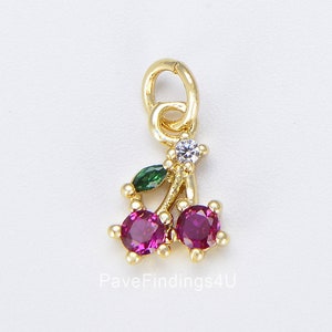 Könnte beinhalten: Goldener Anhänger mit zwei roten Kirschen, grünen Blättern und klaren Strasssteinen. PaveFindings4U ist unter dem Anhänger gedruckt.