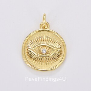 May include: Gold-toned pendant charm featuring a detailed eye design with a clear crystal in the center. The eye is surrounded by radiating lines, creating a sunburst effect.