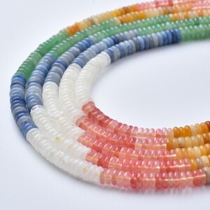May include: Close-up of several strands of colorful gemstone beads. The beads are arranged in a curved pattern, showcasing a spectrum of colors including white, pink, orange, yellow, green, and blue. The beads appear to be small and uniform in size.