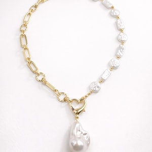 May include: A gold-toned necklace featuring a combination of chain links and irregular-shaped white pearls. A heart-shaped clasp connects the chain to a large, pear-shaped pearl pendant. The necklace is set against a white background.