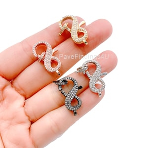 May include: Four infinity-shaped clasps with pave-set clear rhinestones. The clasps are in gold, rose gold, silver, and black.