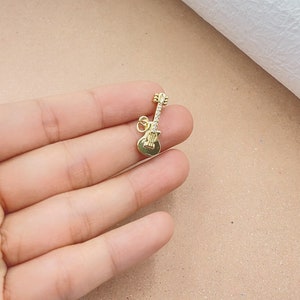 May include: A gold-colored guitar charm with clear rhinestones. The charm is small and detailed, perfect for adding a musical touch to jewelry.