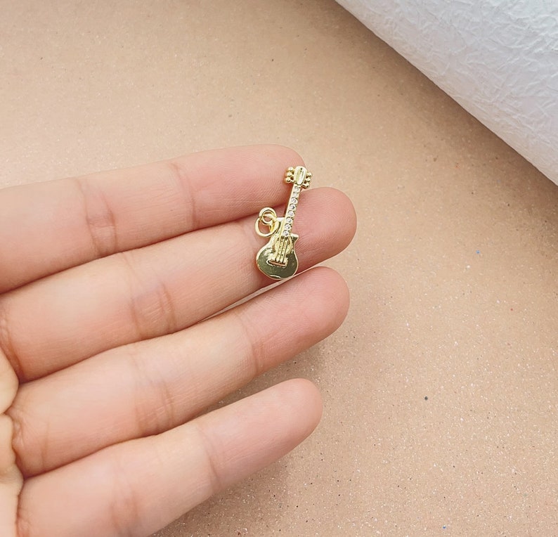 May include: A gold-colored guitar charm with clear rhinestones. The charm is small and detailed, perfect for adding a musical touch to jewelry.