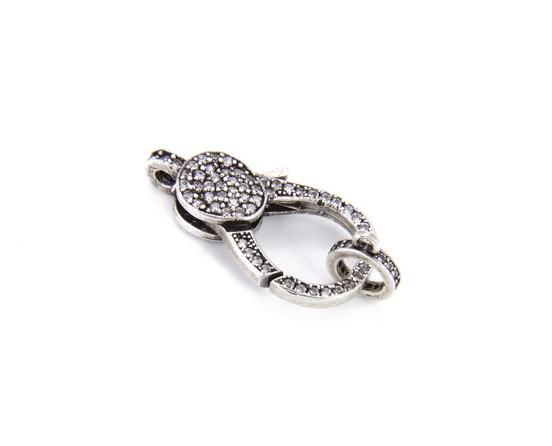 May include: Silver-toned clasp with a round, clear crystal-encrusted top. The clasp is designed for jewelry making.