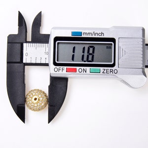 May include: A gold-toned bead with clear rhinestones is measured with a digital caliper. The caliper reads 11.8 mm.