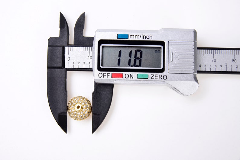 May include: A gold-toned bead with clear rhinestones is measured with a digital caliper. The caliper reads 11.8 mm.