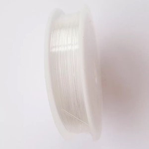 Puede incluir: Una bobina de hilo el&aacute;stico transparente para hacer joyas. El hilo est&aacute; enrollado alrededor de una bobina de pl&aacute;stico blanca.