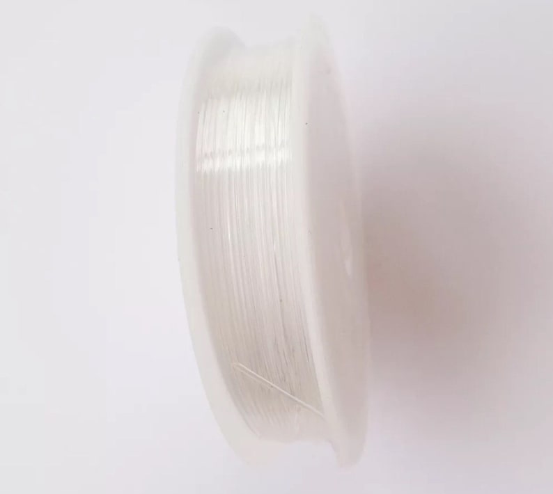 Puede incluir: Una bobina de hilo el&aacute;stico transparente para hacer joyas. El hilo est&aacute; enrollado alrededor de una bobina de pl&aacute;stico blanca.