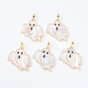 May include: Five ghost-shaped pendants with gold-colored trim and bails. The ghosts are white with black eyes and mouths. The pendants have a pearlescent, iridescent finish, and are set against a white background.