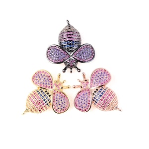 May include: Three bee charms with colorful rhinestones. The bee charms are made of metal and have a gold, rose gold, and black finish. The bee charms are perfect for jewelry making.