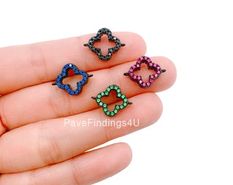 May include: Four black metal clover charms with different colored crystal accents. The charms are blue, green, pink, and black.