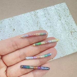 May include: Four small, rectangular jewelry connectors with rainbow-colored gemstones. The connectors are in gold, silver, and black tones. Each connector has a small loop on each end for attaching to other jewelry components.