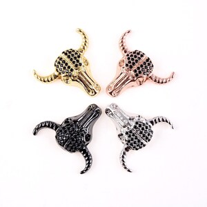 May include: Four metal bull skull charms with black rhinestone accents. The charms are in gold, silver, black, and rose gold.