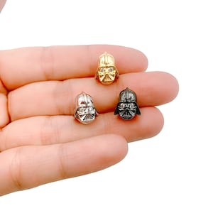 May include: Four small, metallic Darth Vader helmet charms in gold, silver, and black. Each charm features a detailed design of the iconic helmet, with clear crystal accents on the face. These charms are ideal for jewellery making or crafting.