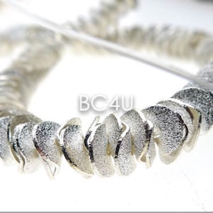 May include: Silver-toned metal chain with a textured finish. The chain is made up of small, curved links that are twisted together. The chain is in the shape of a circle.