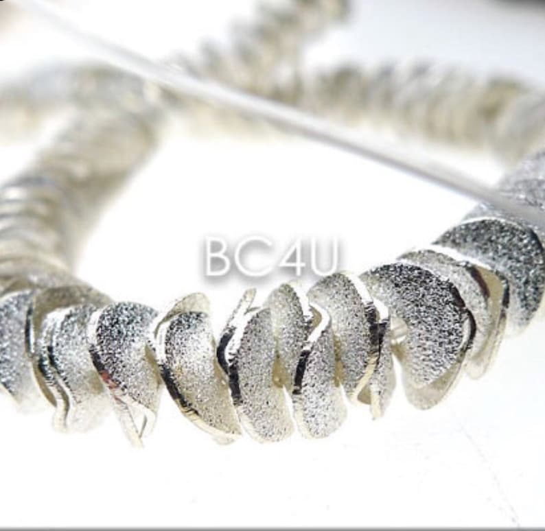 May include: Silver-toned metal chain with a textured finish. The chain is made up of small, curved links that are twisted together. The chain is in the shape of a circle.