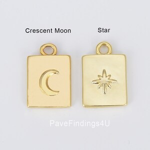 May include: Two gold-toned metal charms, one shaped like a crescent moon and the other shaped like a star, both with a square frame. The charms are on a white background.