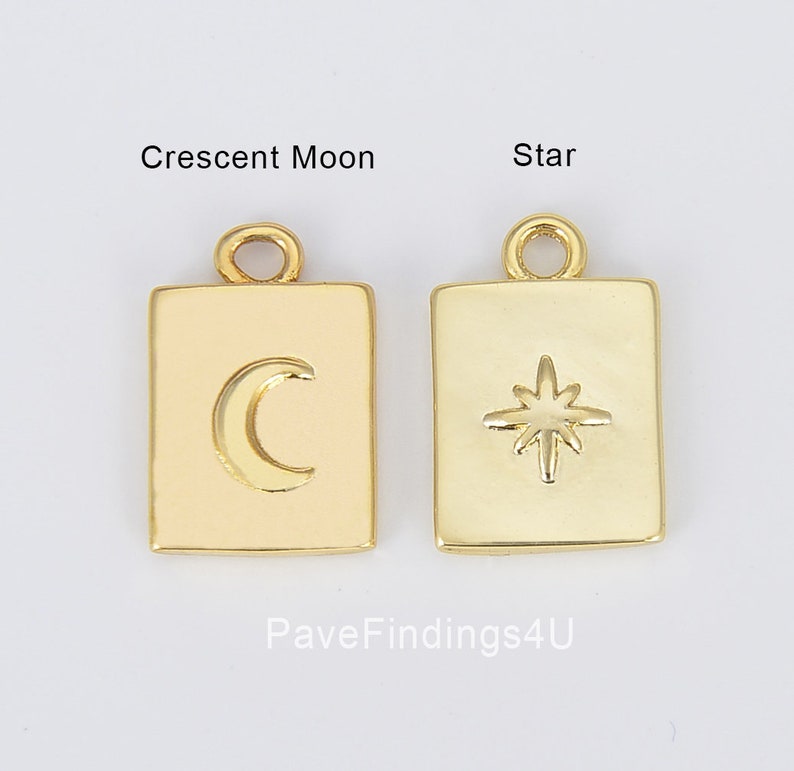 May include: Two gold-toned metal charms, one shaped like a crescent moon and the other shaped like a star, both with a square frame. The charms are on a white background.