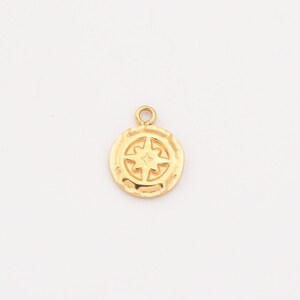 May include: A gold-colored pendant with a compass rose design. The round charm has a textured surface and a small loop at the top for attaching to a chain or bracelet. The compass rose features a central star.