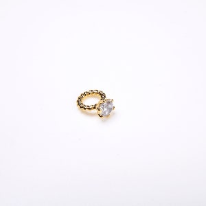 May include: A gold-coloured ring featuring a large, clear, round gemstone. The ring band has a textured, twisted design. The ring is set against a plain white background.