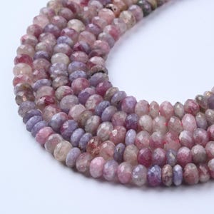 May include: Strands of faceted gemstone beads in shades of pink, purple, and lavender. The beads have a slightly irregular shape and a polished, sparkling surface. The beads are strung together, creating a necklace or bracelet.