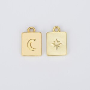 May include: Two gold-toned metal charms, each with a square shape and a raised design. One charm features a crescent moon, the other a star.