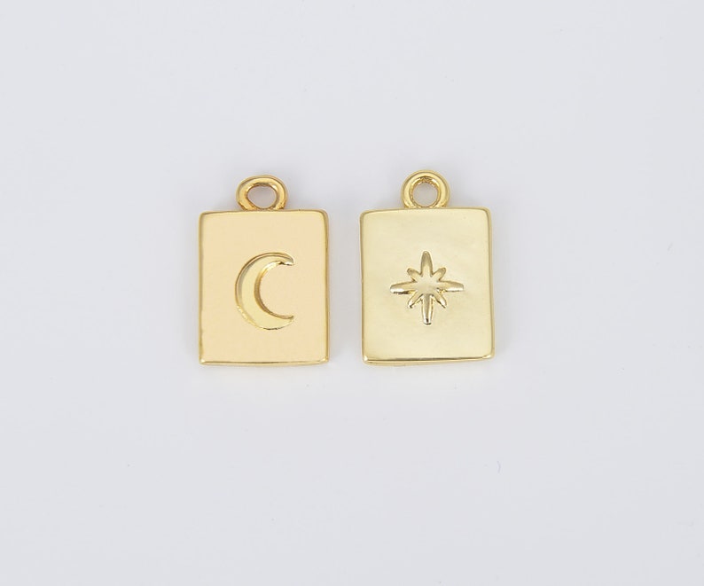 May include: Two gold-toned metal charms, each with a square shape and a raised design. One charm features a crescent moon, the other a star.