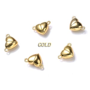 May include: Five gold heart-shaped magnetic clasps for jewelry making. The clasps are made of metal and have a shiny finish.