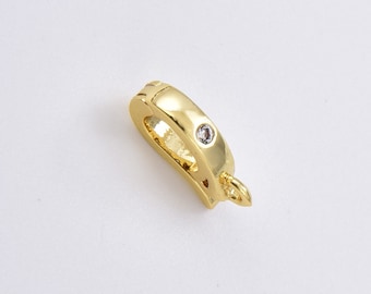 May include: A gold-toned metal jewelry clasp featuring a smooth, curved design with a single small, clear, round-cut gemstone embedded on the top surface and a small circular loop attached to one end for connecting to chains or pendants.