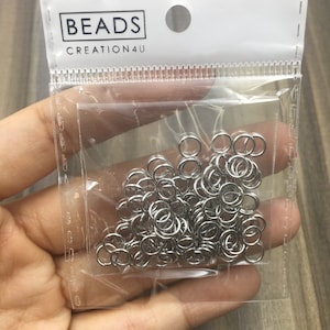 May include: A clear plastic bag filled with silver jump rings. The bag has a white label with the text "BEADS CREATION4U".