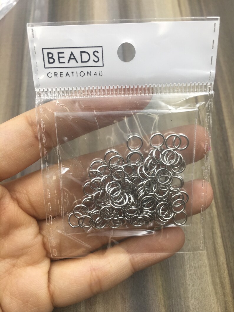 May include: A clear plastic bag filled with silver jump rings. The bag has a white label with the text "BEADS CREATION4U".