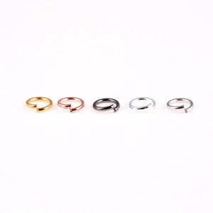 May include: Five jump rings in different colors: gold, rose gold, black, silver, and gunmetal. The rings are all the same size and are arranged in a row.